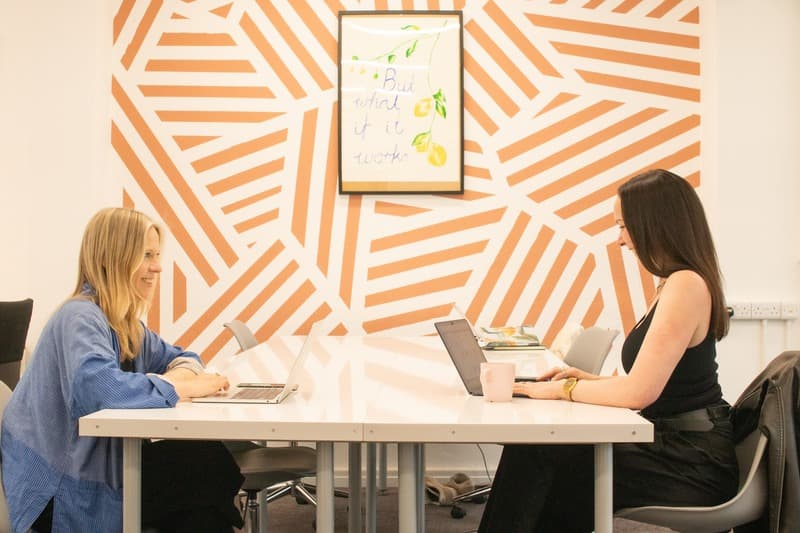 Two members working at hot desks in front of WILDHeart's orange striped mural